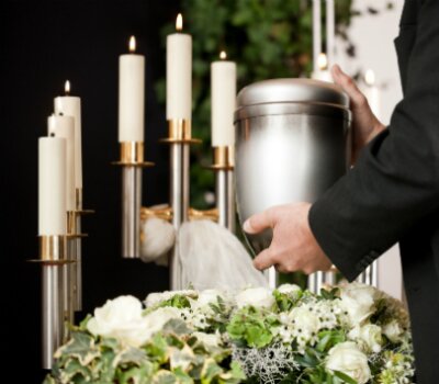 silver cremation urn at a service with white tapers and flowers